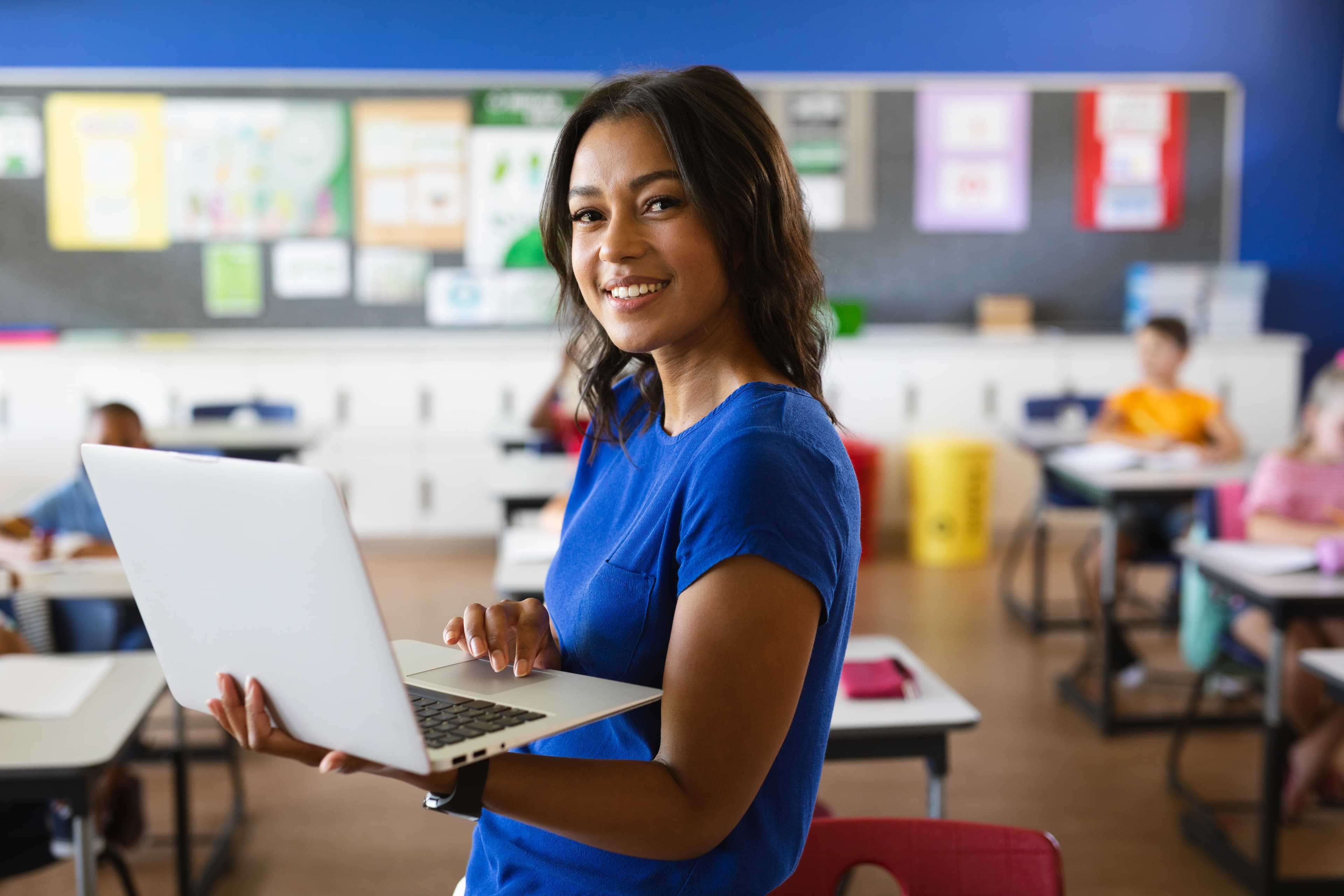 Image of a female teaching holding a laptop in a classroom