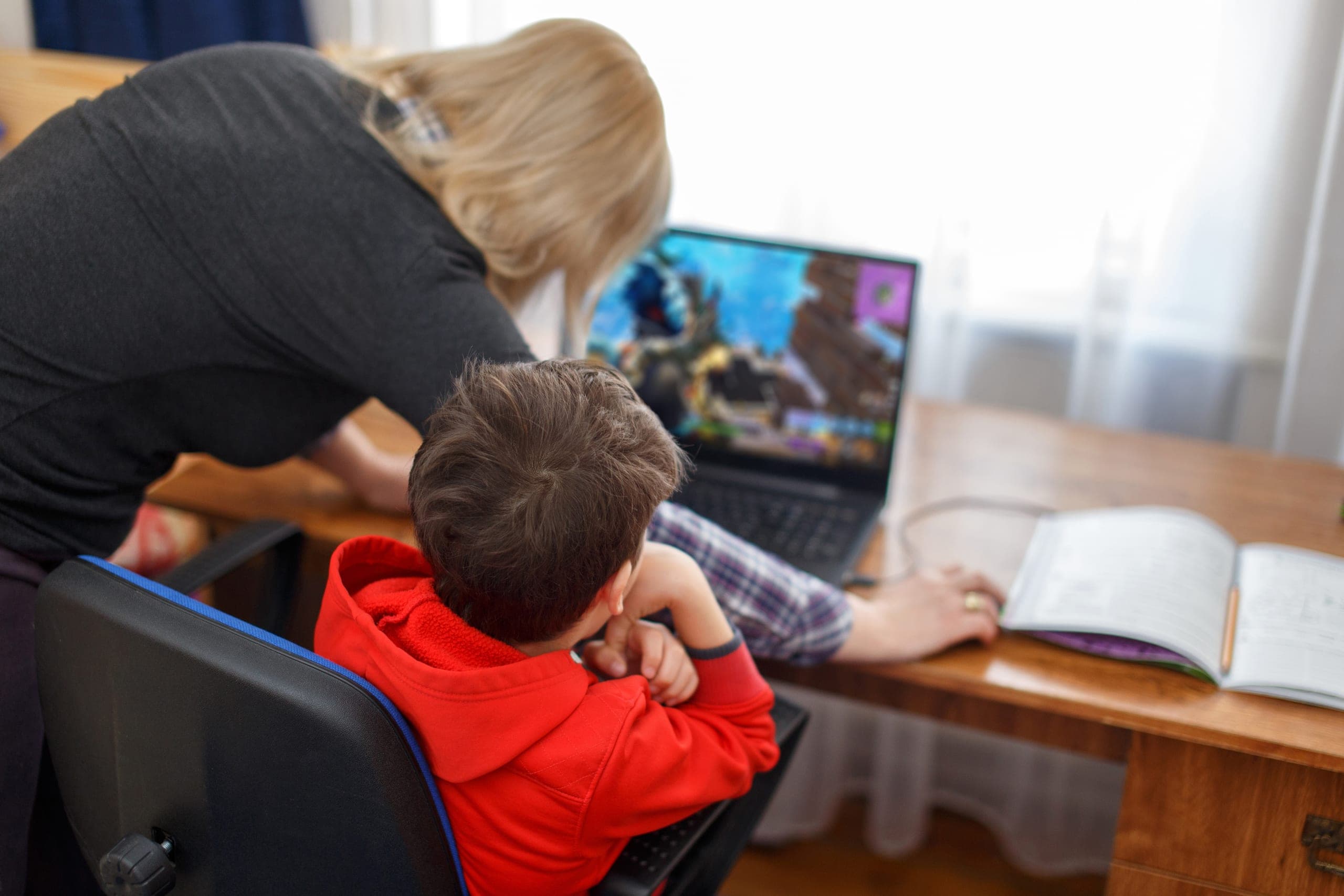A woman standing behind a child sitting in front of a computer open to a gaming platform